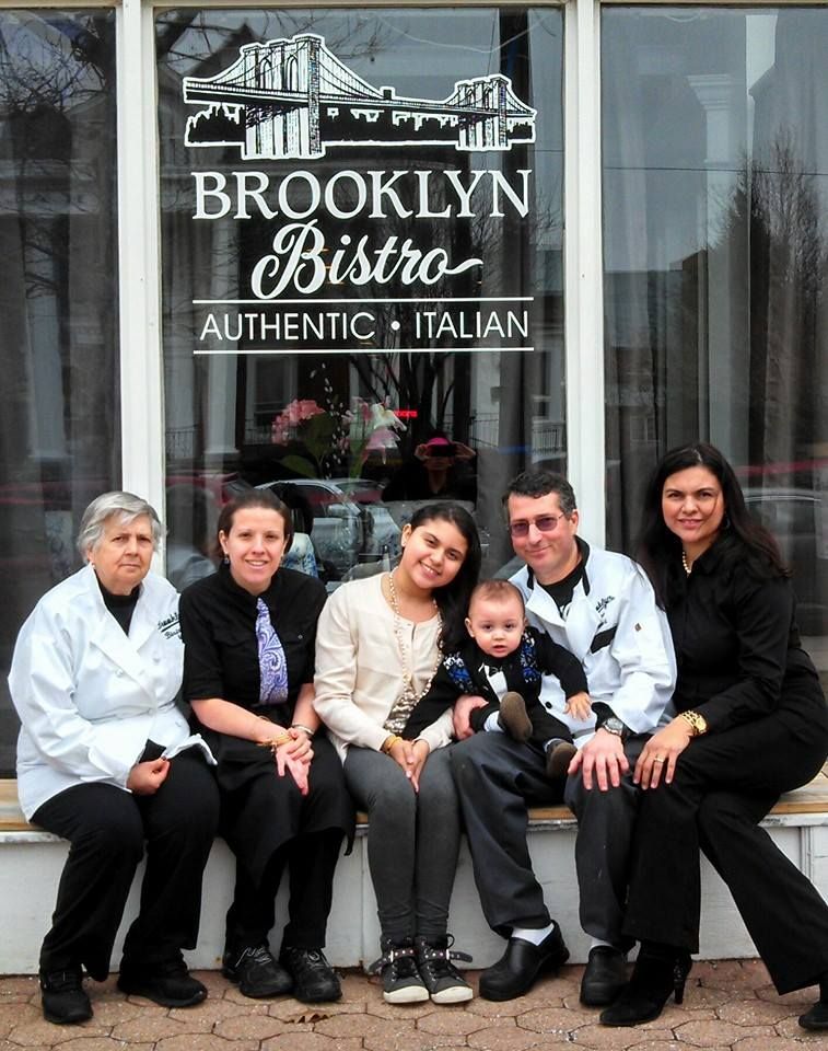 Brooklyn Bistro staff posing outside, with a baby in the center. Restaurant sign above.
