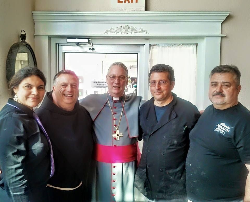 Group of five people posing by a door. A cleric in vestments stands in the center with others.