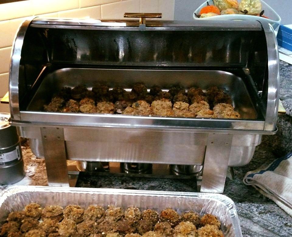 A stainless steel chafing dish holds meatballs, with a full tray in the foreground.