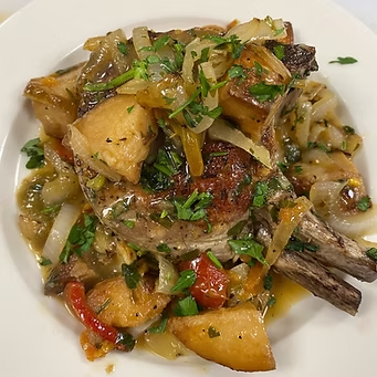 Pork chop with potatoes, onions, and sauce on a white plate, garnished with fresh herbs.