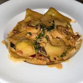 Ravioli with creamy orange sauce, shrimp, and herbs in a white bowl.