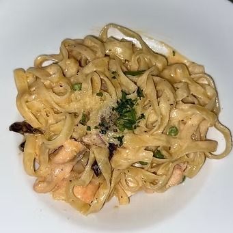 Fettuccine pasta with creamy sauce, garnished with parsley and pepper, served on a white plate.