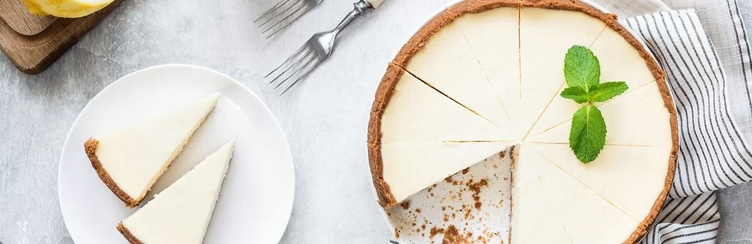 Cheesecake with sliced portions, mint garnish, served on a white plate.