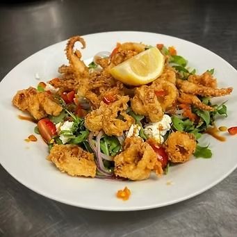Fried calamari and salad with a lemon wedge on a white plate.