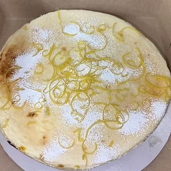 Lemon cheesecake topped with powdered sugar and lemon zest in a cardboard container.