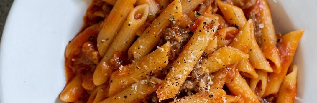 Penne pasta in tomato sauce with seasoning, served in a white bowl.