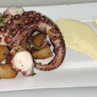 Grilled octopus with potatoes and yellow sauce on a white plate.