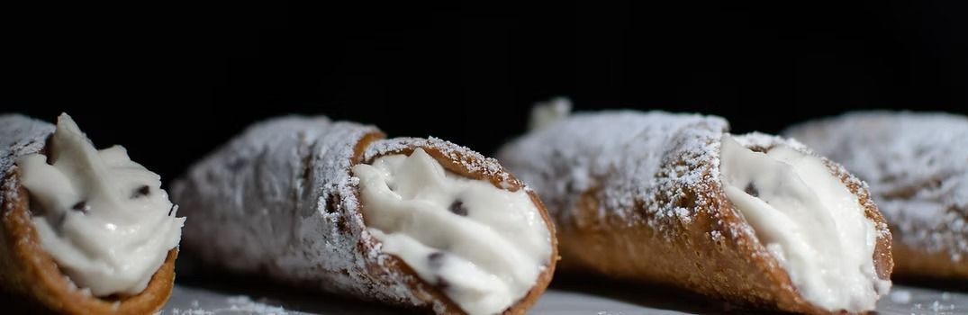 Close-up of several cannoli pastries, dusted with powdered sugar, against a dark background.