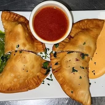 Fried empanadas on a white plate with small bowls of red sauce, green sauce and yellow sauce.