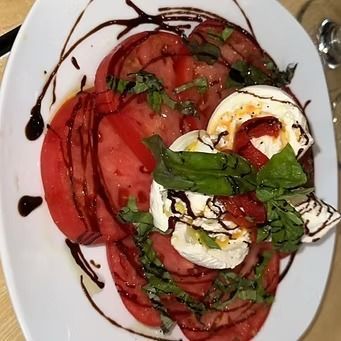 Tomato and mozzarella salad with basil and balsamic glaze on a white plate.