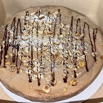 Round cake, light brown frosting, drizzled with chocolate, topped with hazelnuts and powdered sugar.
