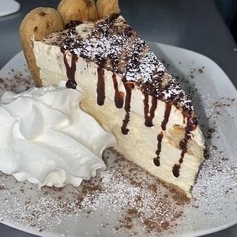 Slice of layered dessert with chocolate drizzle, whipped cream, and cocoa powder on a white plate.