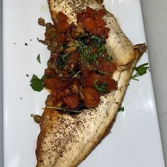 Pan-seared fish fillet topped with tomatoes and herbs on a white plate.