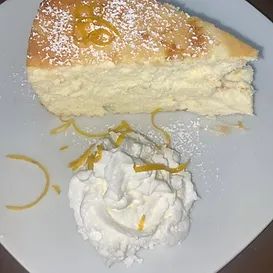 Slice of cheesecake with whipped cream and lemon zest on a white plate.
