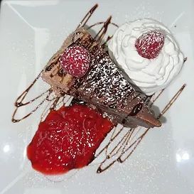 Chocolate dessert with whipped cream and berry compote, drizzled chocolate sauce.