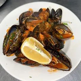 Mussels in sauce on a white plate with a lemon wedge.