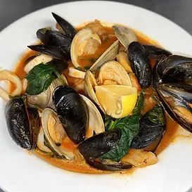 Seafood stew with mussels, clams, squid, and a lemon wedge, in a white bowl.
