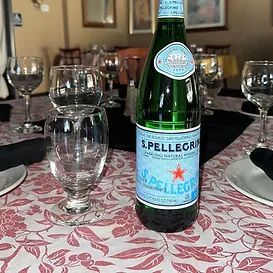 S. Pellegrino bottle on a table set with glasses and floral tablecloth.
