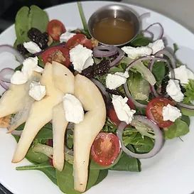 Salad with pears, tomatoes, onions, goat cheese, greens, and dressing in a small dish.
