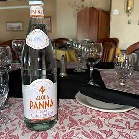 Bottle of Acqua Panna water on a table set for dining, with glasses and floral tablecloth.