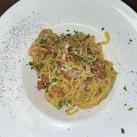 Spaghetti carbonara with bacon, Parmesan cheese, and black pepper on a white plate.