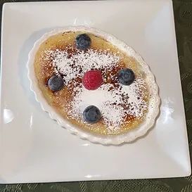 Crème brûlée dessert in a white dish, topped with berries and powdered sugar.