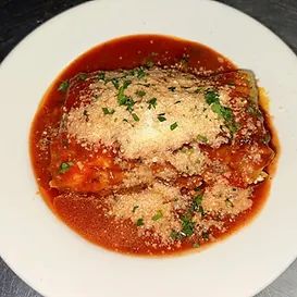 Lasagna roll-up in tomato sauce, topped with grated cheese and parsley, on a white plate.