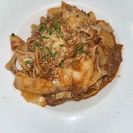 Pasta dish with wide noodles and a meat sauce, topped with grated cheese and parsley, in a white bowl.