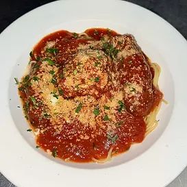 Spaghetti with meatballs, red sauce, and grated cheese on a white plate.