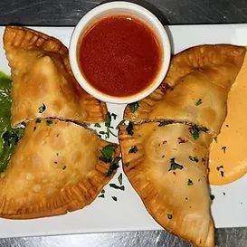 Four golden-brown, fried empanadas on a plate with three dipping sauces: red, green, and orange.