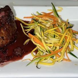 Steak with red sauce, served with spiralized yellow, orange, and green vegetables.