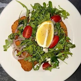 Breaded cutlet with arugula salad, tomatoes, red onion, and lemon on a white plate.