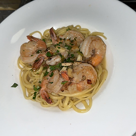 Linguine pasta topped with shrimp, garlic, and parsley, in a white bowl.