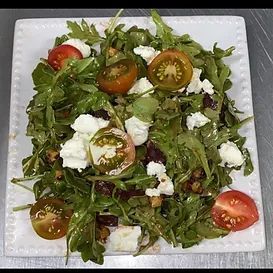 Salad on a square white plate, with arugula, cherry tomatoes, goat cheese, and walnuts.