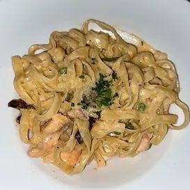 Fettuccine pasta in creamy sauce, garnished with parsley, on a white plate.