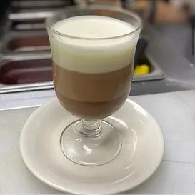 Layered drink in a glass on a saucer; light brown, medium brown, and white layers.