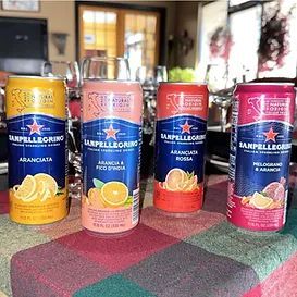 Four Sanpellegrino sparkling fruit beverages in colorful cans, sitting on a table.