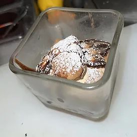 Dessert in a square glass. Round, powdered sugar-dusted pieces with chocolate drizzle.