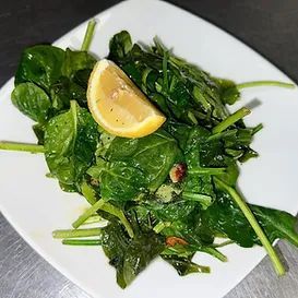Spinach salad with a lemon wedge on a white square plate.