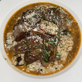 Braised meat over risotto, topped with grated cheese and herbs, in a shallow bowl.