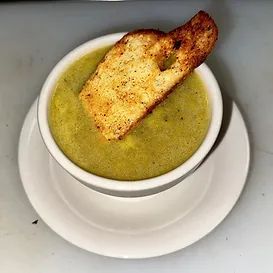 A bowl of green soup with a toasted bread slice on a white plate.