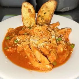 Tripe stew in red sauce with peas, topped with breadcrumbs, served with garlic bread.