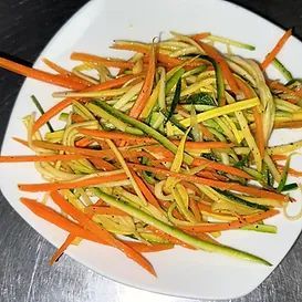 Colorful julienned vegetables (carrots, zucchini) on a white plate.