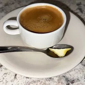 Cup of coffee on saucer with spoon holding a lemon wedge.