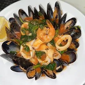Seafood stew with mussels, shrimp, and calamari in tomato sauce on a white plate with lemon.