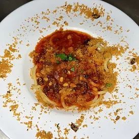 Spaghetti dish with tomato sauce, pine nuts, and breadcrumbs, on a white plate.
