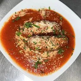 Two breaded and sauced food items in a white bowl with grated cheese and chopped herbs.