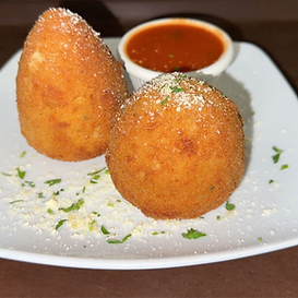 Two golden-brown, fried arancini with a side of red sauce, garnished with parsley and grated cheese on a white plate.