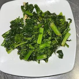 Plate of cooked green vegetables, possibly broccoli rabe, on a white plate.