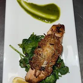 Salmon fillet with crispy topping on spinach, drizzled with green sauce, served on a white plate.
